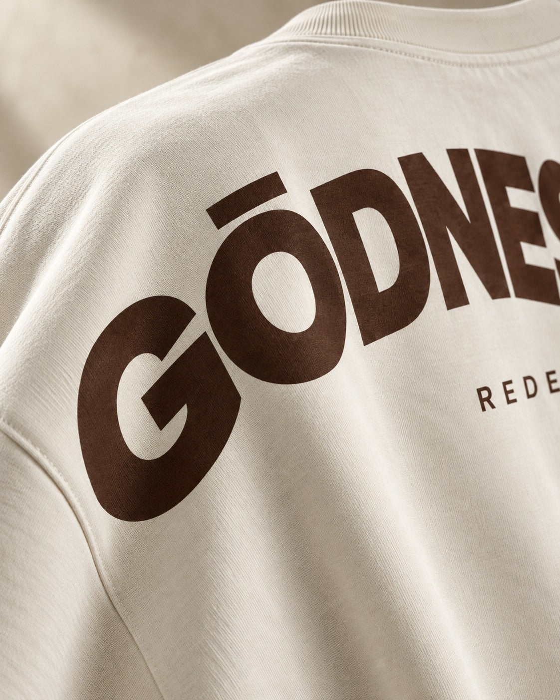 Teaser concept: an angled crop of the bone T-shirt's rear shoulder reveals part of the coffee-brown screen print.